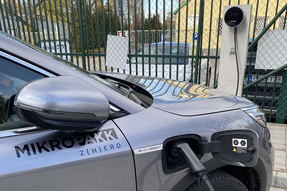 Sustainable development in the plastics industry, smiling electric car charger in front of the Mikropakk facility.